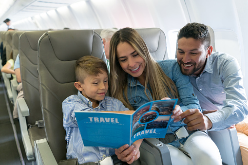 Portrait of a happy family traveling by plane and reading a travel guide - lifestyle concepts.