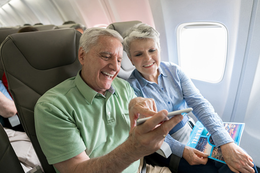 Happy senior couple traveling by plane and using their cell phone onboard on airplane mode - lifestyle concepts