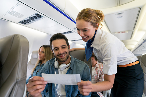 Portrait of a happy flight attendant checking a manâs seat and her boarding pass in the plane