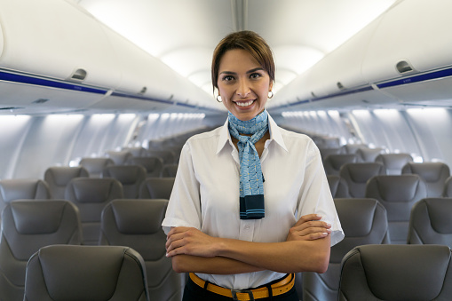 Portrait of a beautiful air hostess in an airplane looking at the camera smiling - travel concepts