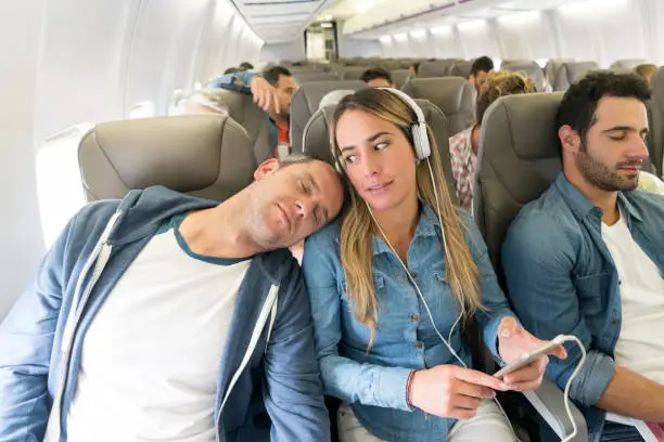 Rude man sleeping on a passenger's shoulder in an airplane while traveling by air - lifestyle concepts