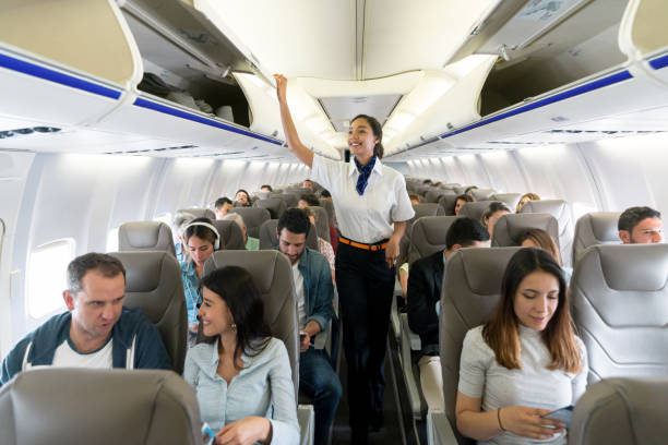 atendente de voo feliz caminhando pelo corredor em um avião fechar compartimentos - passenger - fotografias e filmes do acervo