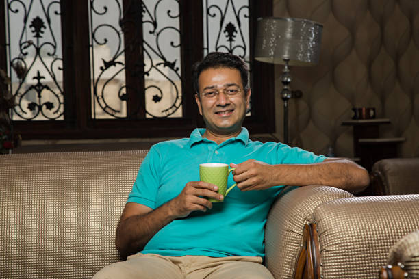 istock Attractive cheerful young man having coffee on sofa - Stock image 1028472064