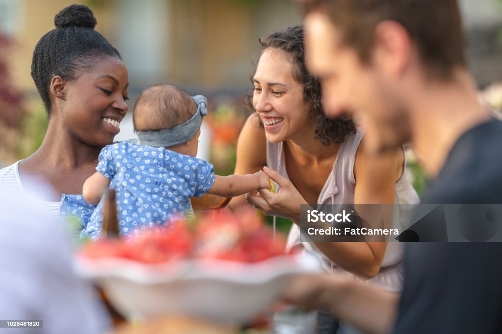 A group of young adult friends dining al fresco on a patio A young African American mom holds her adorable young daughter in her lap at an outdoor dining table. The girl is smiling and reaching toward mom's friend, who's smiling at her. Community Stock Photo