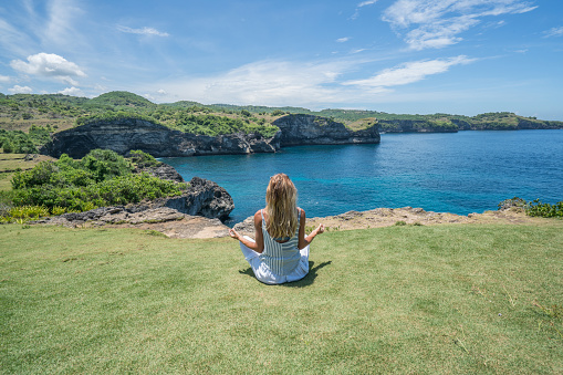 Young woman exercising yoga on rock coastline in Nusa Penida Island near Bali, people travel relaxation concept in nature