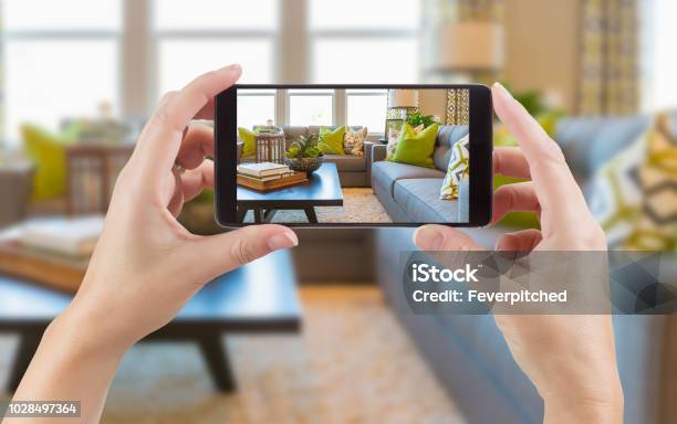 Female Hands Holding Smart Phone Displaying Photo Of House Interior Living Room Behind Stock Photo - Download Image Now