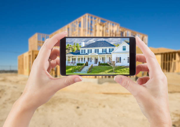 mujer manos sosteniendo elegante teléfono mostrar foto de casa con construcción sin terminar detrás de. - solar de construcción fotos fotografías e imágenes de stock