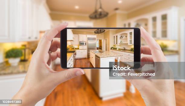 Female Hands Holding Smart Phone Displaying Photo Of Kitchen Behind Stock Photo - Download Image Now