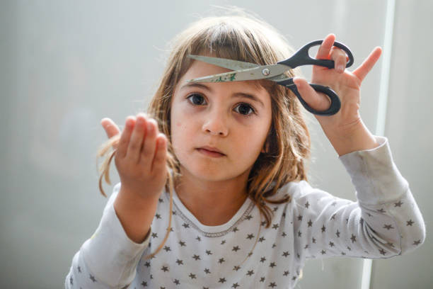 The Haircut. Cute little 4 year old girl holds a pair of scissors in one hand and the hair she cut from her head in the other hand. child behaving badly stock pictures, royalty-free photos & images
