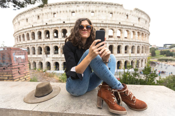 femme souriante, à l’aide d’un téléphone intelligent en face du colisée - international landmark italy amphitheater ancient photos et images de collection