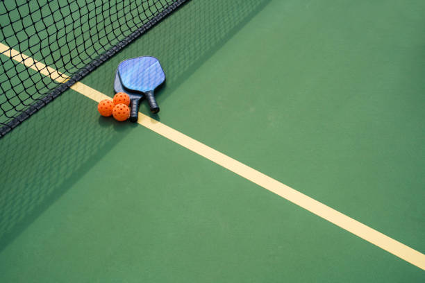 Pickleball paddles and ball in shadow of net Pickleball paddles and ball on court with shadow of net ++graphics on paddles was created by photographer and is copyright free ++ pickleball stock pictures, royalty-free photos & images