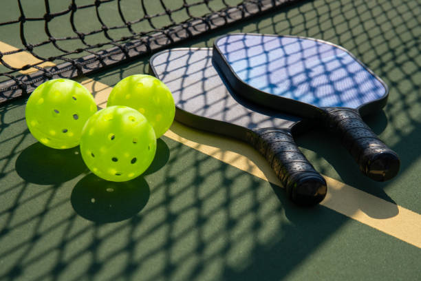Pickleball paddles and ball in shadow of net Pickleball paddles and ball on court with shadow of net ++graphics on paddles was created by photographer and is copyright free ++ pickleball equipment stock pictures, royalty-free photos & images