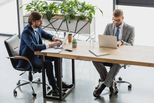 istock high angle view of young businessmen in suits using laptops and working together in office 1028602388