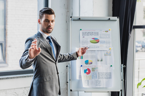 young businessman pointing at whiteboard with business charts and graphs