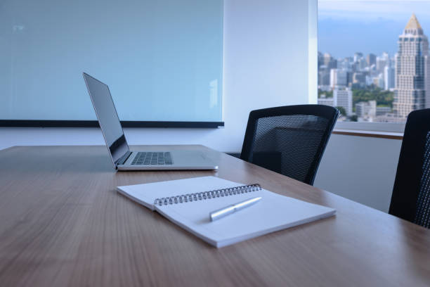 istock Laptop and pen on notepad for agenda kept on table in empty corporate conference room with cityscape view on background. selected focus on laptop. 1028622928