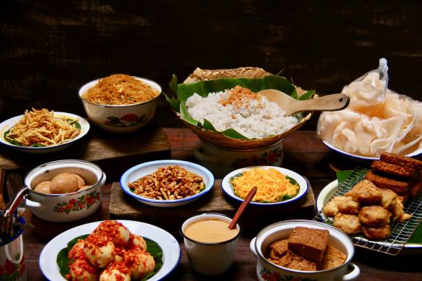 Nasi Uduk Betawi, the Traditional Street Food of Savoury Rice Dish from Betawi, Jakarta Nasi Uduk Betawi, the popular street food dish of rice cooked in coconut milk with variety of side dishes, such as Omelette Strips, Potato Crisps, Tempe Crisps, Fried Vermicelli, Eggs in Crushed Chili Paste, Braised Eggs and Tofu in Soy, Potato Patties, Fried Tempeh. Accompanied with some crackers and condiment of spicy peanut sauce. The dishes, except the rice, are plated on vintage enamel crockery; while the rice is served on a woven bamboo cone. Indonesia food stock pictures, royalty-free photos & images