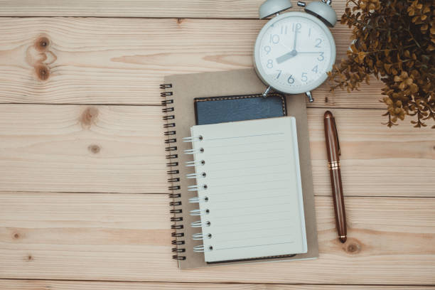 istock Office supplies or office work essential tools items on wooden desk in workplace, pen with notebook and alarm clock, top view 1028650608