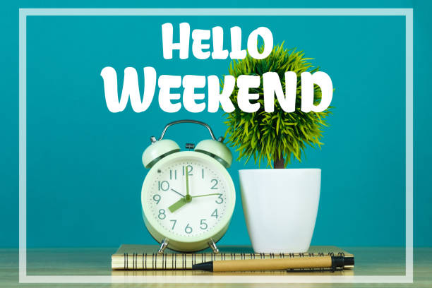 istock Hello Weekend text on green background and little tree with vintage alarm clock and notebook paper pen on wooden table 1028652496