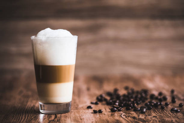 Caffe latte layered Caffe latte layered with milk in a high drinking glass. There are roasted coffee beans spread out on the wooden table next to the glass, and the background is also wooden. cafe macchiato stock pictures, royalty-free photos & images