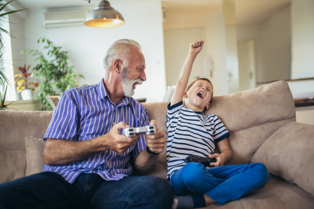 nonno e nipote stanno giocando ai videogiochi a casa. - video game family child playful foto e immagini stock