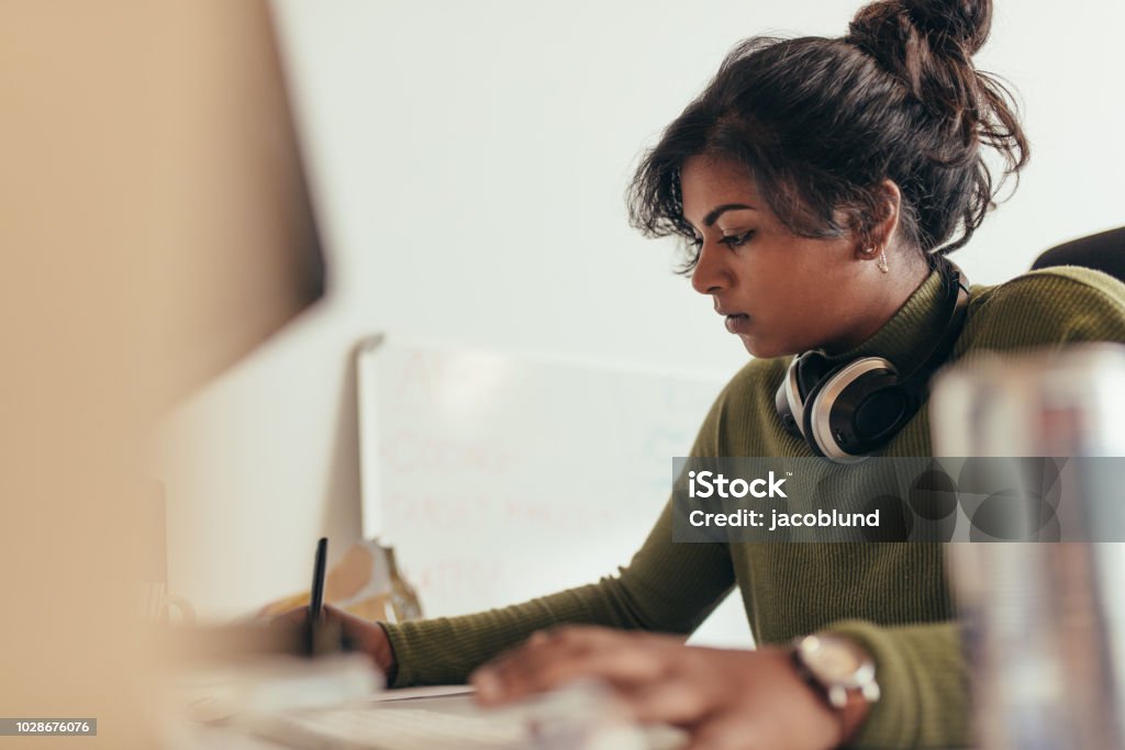 Female computer programmer working at her desk Woman making notes while working on computer. Female computer programmer working at her desk. India Stock Photo