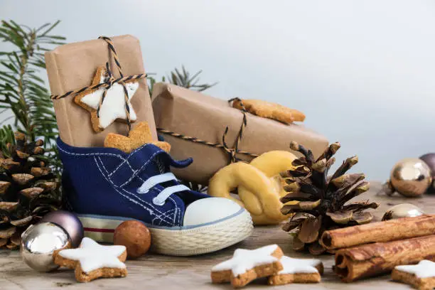 Children's shoe with sweets, gifts and christmas ornaments on rustic wood, german text Am 6. Dezember ist Nikolaustag, meaning  St. Nicholas Day December 6th, selected focus, narrow depth of field