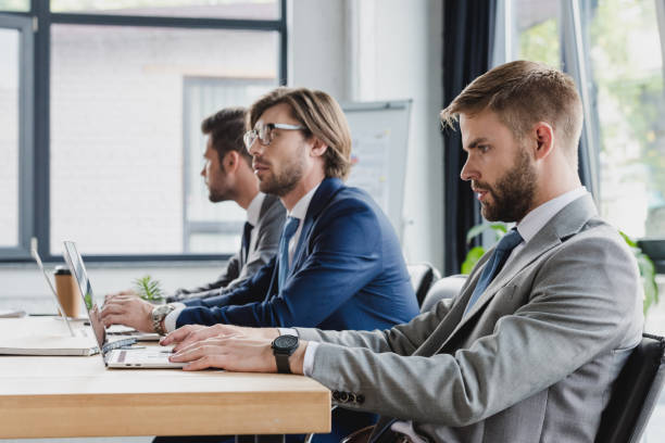 istock side view of three focused young businessmen using laptops at workplace 1028703718