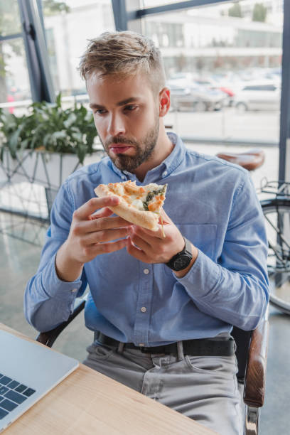 istock handsome young businessman eating pizza in office 1028704204
