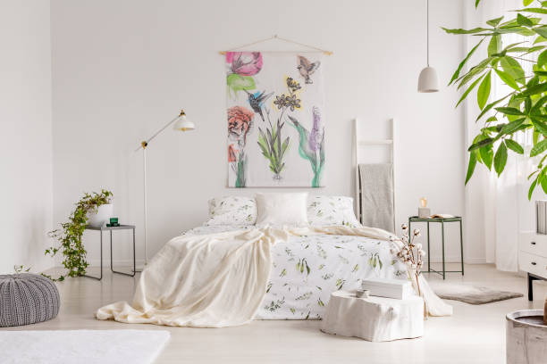 istock A bright eco friendly bedroom interior with a bed dresses in green plants pattern white linen. Fabric painted in flowers and birds on the background wall. Real photo. 1028745588
