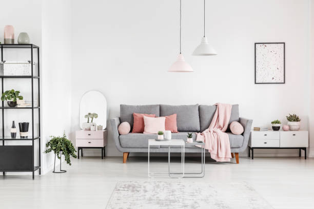 istock Tables in front of grey couch between cabinets in white flat interior with lamps and poster. Real photo 1028748500