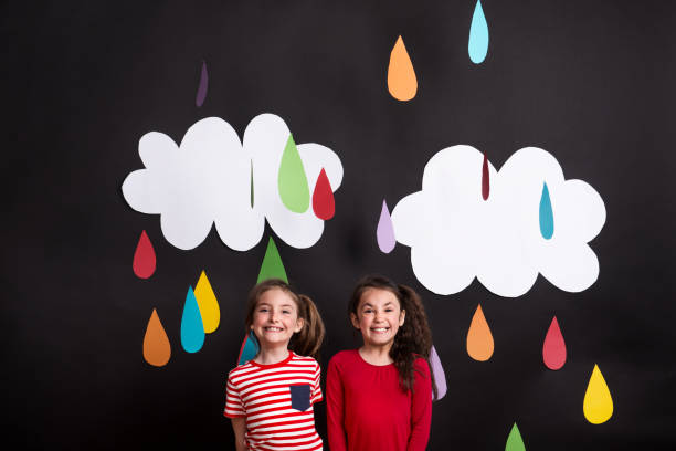 istock Small girls in studio, standing against black background with clouds and raindrops. 1028754128