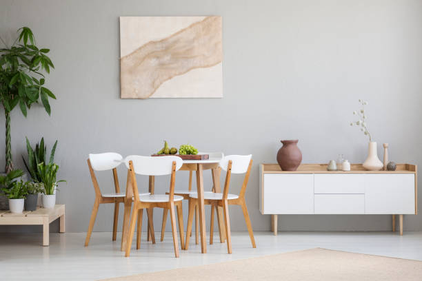 istock White wooden chairs at table between plants and cupboard in grey flat interior with poster. Real photo 1028754416