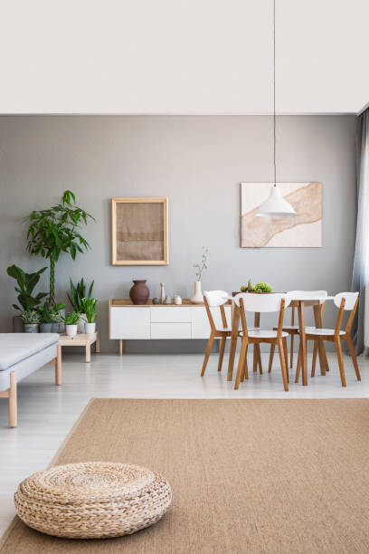 istock Pouf on brown carpet in spacious grey flat interior with chairs at table and posters on the wall. Real photo 1028754434