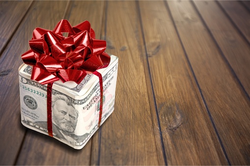Christmas present with red bow wrapped in dollar banknotes isolated on white background