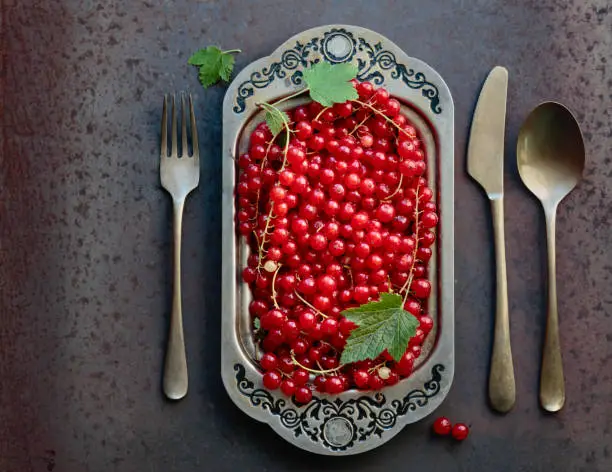 Redcurrants on a metal dish with fork , spoon and knife. Concept for healthy eating, dieting and antioxidant. Top view.