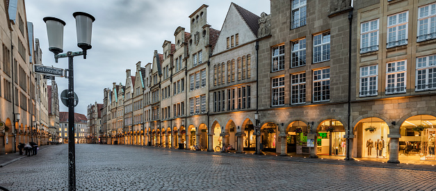 Gallery with arcades on the Prinzipalmarkt in Münster\n,shaped by historic buildings  The Prinzipalmarkt is the historic principal marketplace of Münster, Germany. Shot at dusk. Buildings already illuminated.