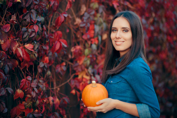 cheerful woman in autumn leaves decor holding a pumpkin - fashion women denim farm imagens e fotografias de stock