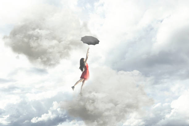 momento surrealista de una elegante mujer volando en medio de las nubes colgando en su paraguas - white mid air rain wind fotografías e imágenes de stock