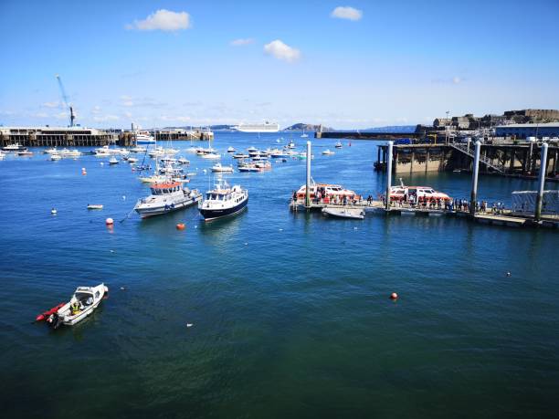 Saint Peter Port is the capital of Guernsey as well as the main port. Boats are moored in the marina on a calm blue sky day.