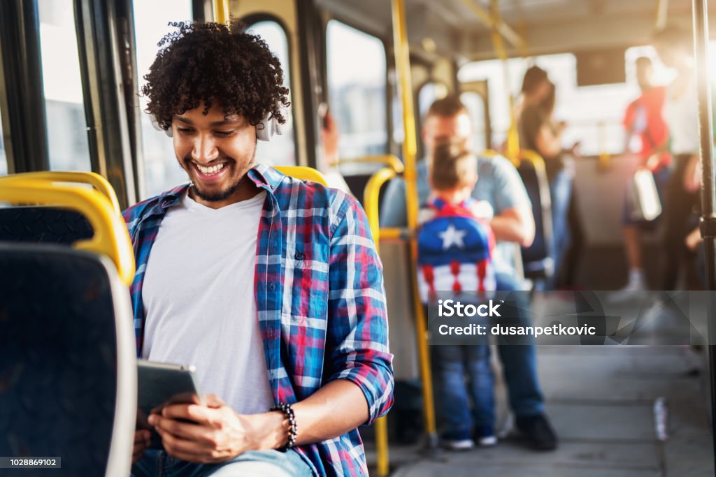 Happy handsome Afro-American man sitting in a bus and listening to the music. Bus Stock Photo