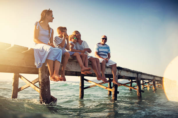 familie sitzt am pier am meer - travel travel destinations outdoors horizontal stock-fotos und bilder