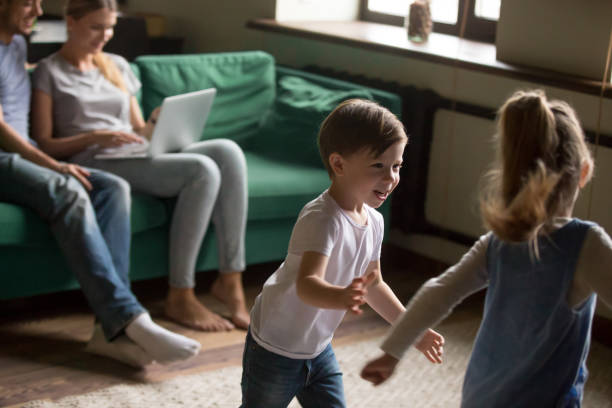 istock Happy kids playing while parents relaxing with laptop at home 1028900380