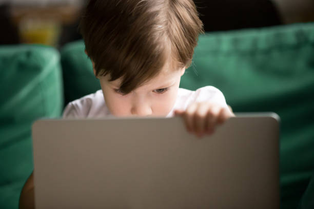 curious kid boy secretly watching forbidden censored content on laptop - segredo criança imagens e fotografias de stock