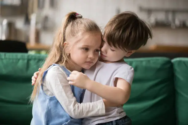 Photo of Little boy brother consoling and supporting upset girl embracing sister