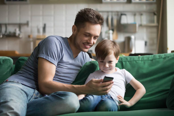 istock Smiling dad with kid son watching funny video on phone 1028900454