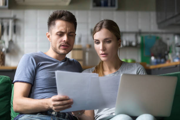 Serious confused couple checking domestic bills with papers and laptop Serious confused couple checking high domestic bills with papers and laptop, millennial family discussing expenses or financial problems bankruptcy debt loan reading bad news in bank documents past due stock pictures, royalty-free photos & images