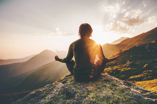 Man meditating yoga at sunset mountains Travel Lifestyle relaxation emotional concept adventure summer vacations outdoor harmony with nature stock photo
