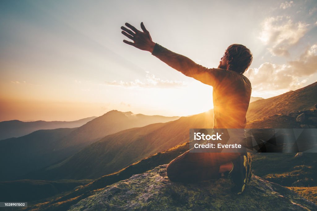 Hombre orando en la montañas al atardecer las manos levantadas viajes vida relajación espiritual emocional concepto vacaciones al aire libre armonía con el paisaje de la naturaleza - Foto de stock de Rezar libre de derechos