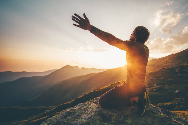 Man praying at sunset mountains raised hands Travel Lifestyle spiritual relaxation emotional concept vacations outdoor harmony with nature landscape stock photo