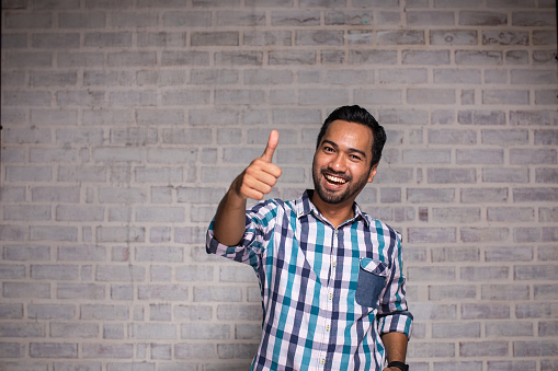 Portrait of happy Malaysian man indoors with thumb up,laughing